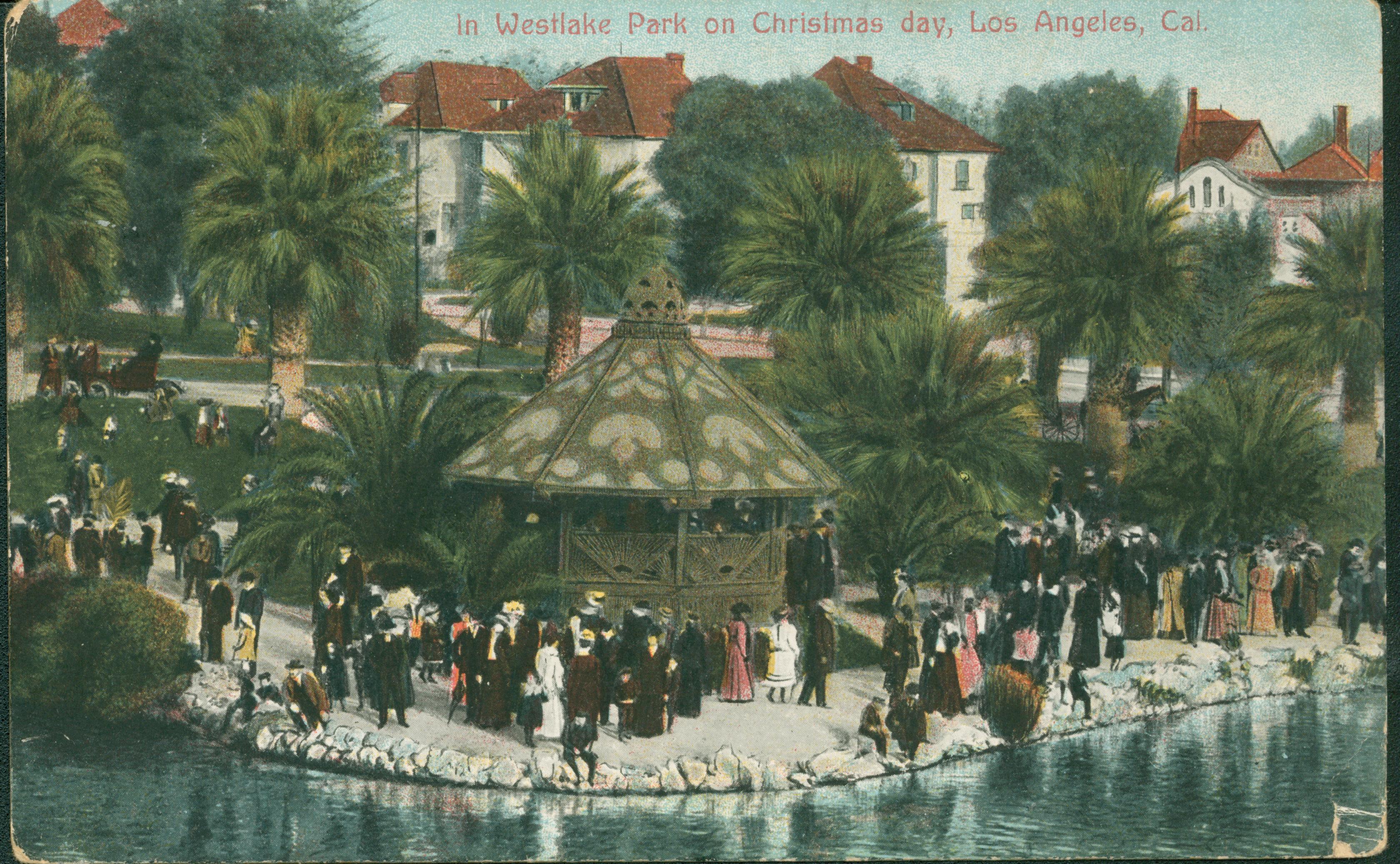 This postcard shows numerous people out strolling along the shores of a lake, past a gazebo